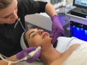 Esthetician using HydraFacial MD facial treatment on client's cheek