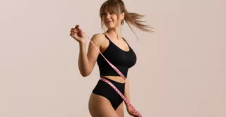A smiling woman measures her waist after weight loss injections
