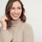 A smiling woman in a beige sweater against a neutral background