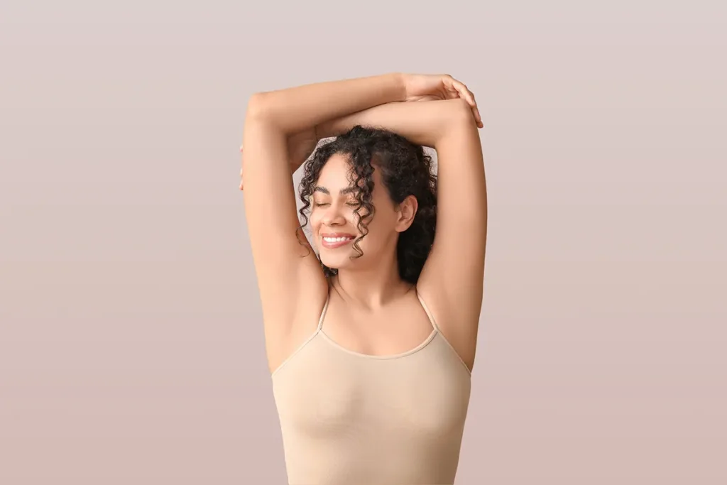 A smiling young woman raises her arms above her head with confidence due to hyperhidrosis treatment, or excessive sweating