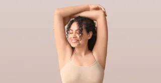 A smiling young woman raises her arms above her head with confidence due to hyperhidrosis treatment, or excessive sweating